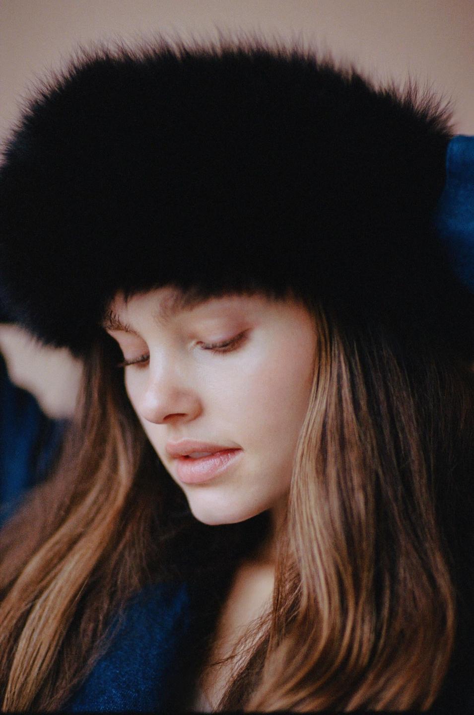 A woman with long hair and a fur hat looks down.