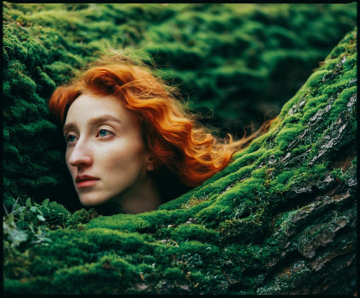 A woman with red hair is nestled in a bed of green moss.