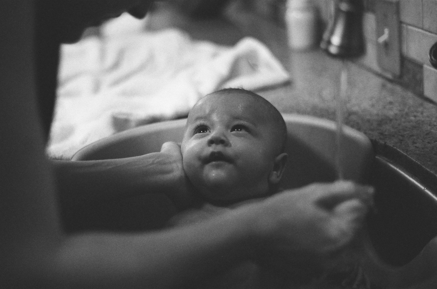 A baby is being bathed in a sink by an adult.