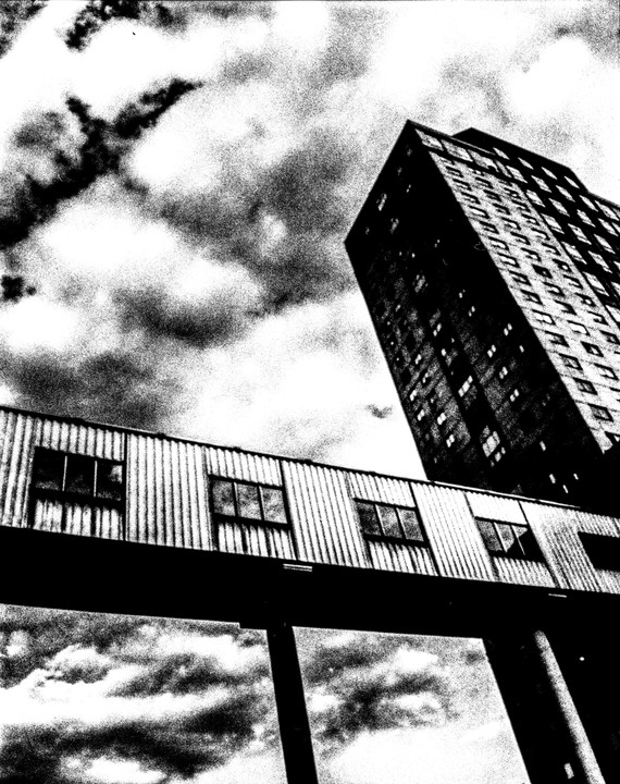 A tall building and a corrugated metal walkway are seen from below against a cloudy sky.