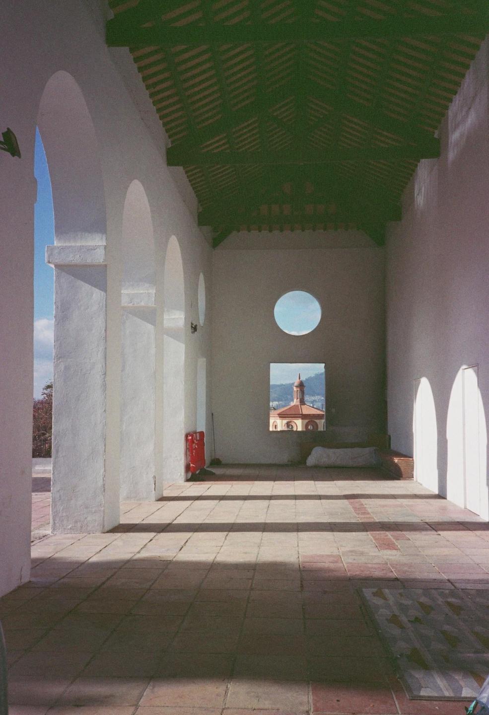 A long, white-walled hallway with a green ceiling leads to a window looking out at a building with a dome.