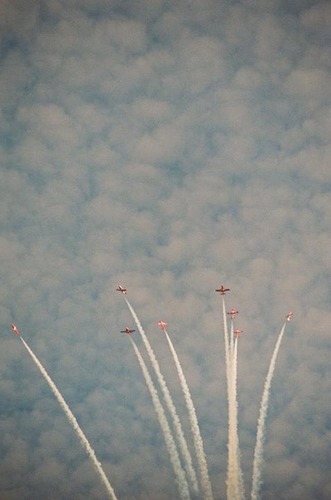Several small airplanes fly in formation, leaving white contrails against a cloudy sky.