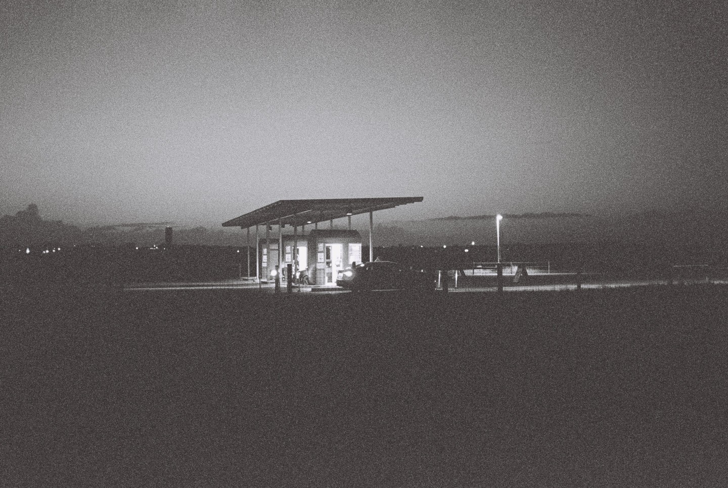 A gas station with a car and a street light is visible in the distance at night.