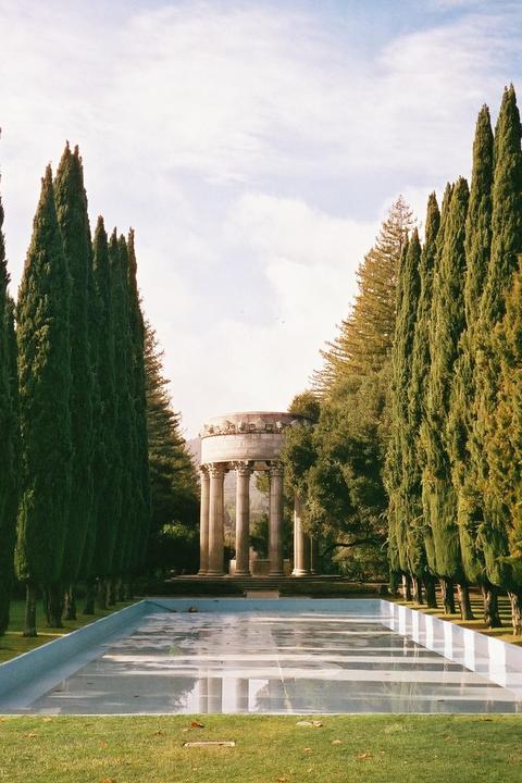 A classical rotunda with columns stands at the end of a reflecting pool, flanked by tall cypress trees.