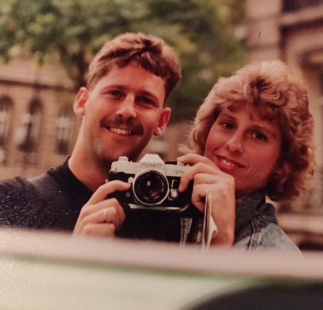 A couple smiles at the camera while holding a camera.
