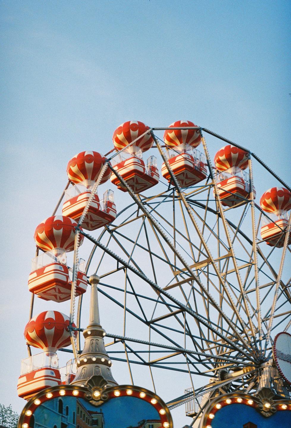A ferris wheel with red and white striped gondolas is set against a clear blue sky.