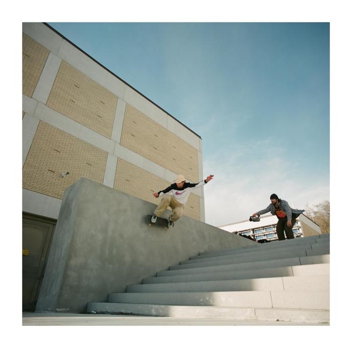 A skateboarder grinds on a concrete ledge while another man films him on a sunny day.