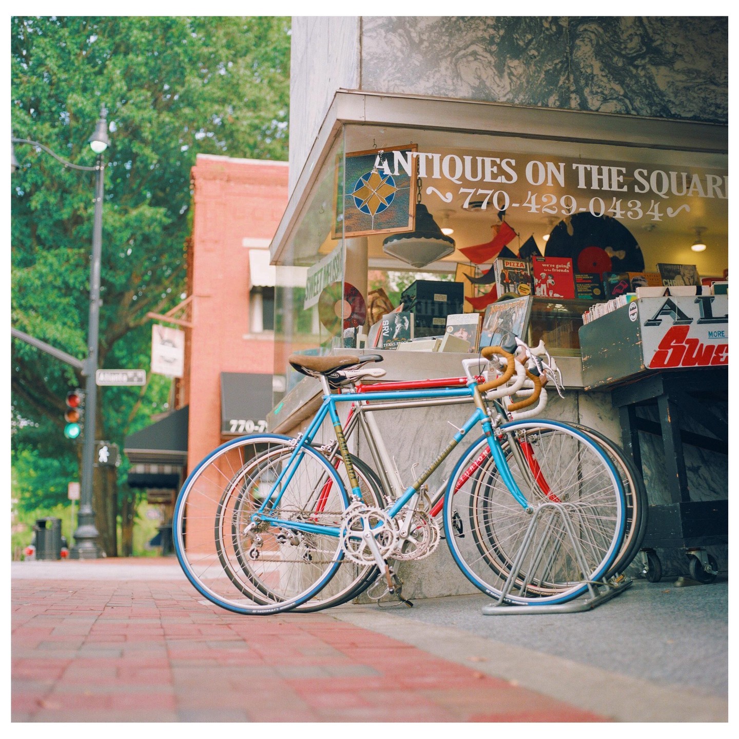 Two bicycles are parked on a brick sidewalk in front of an antique shop.