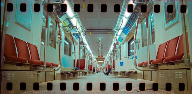 The interior of a subway car with red seats and a person's legs visible in the distance.