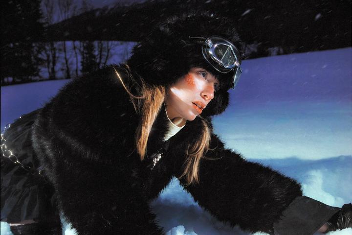 A woman in a fur hat and goggles is in the snow at night.