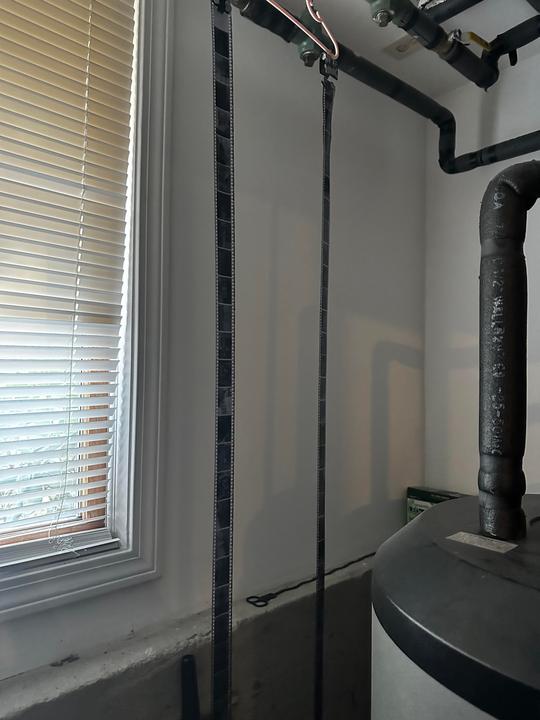 Two strips of developed film hang to dry in a room with a window and a water heater.