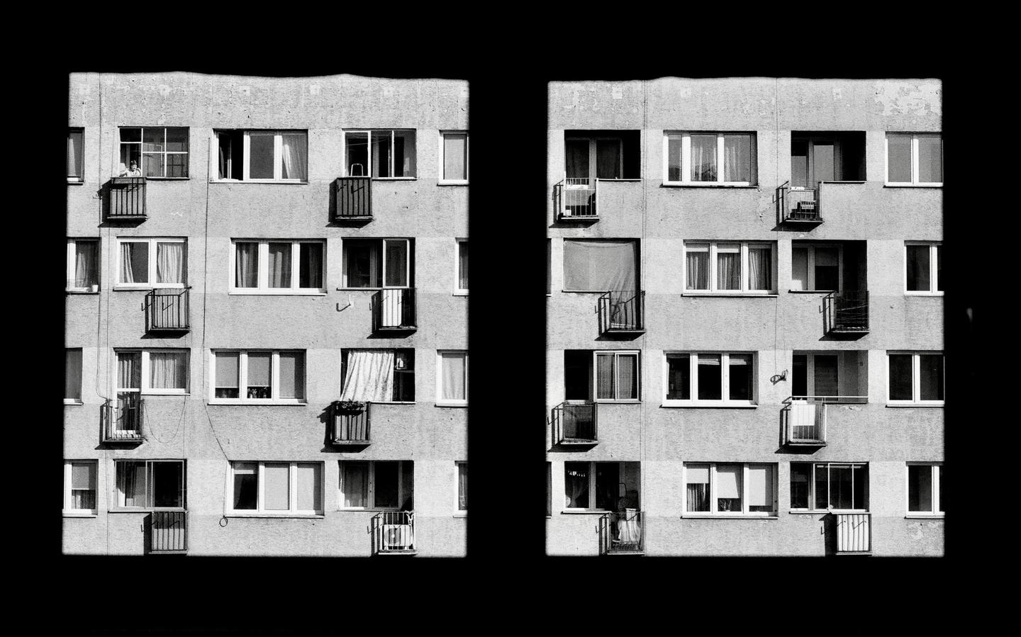 Two sections of a multi-story building facade with many windows and balconies are separated by a black vertical strip.