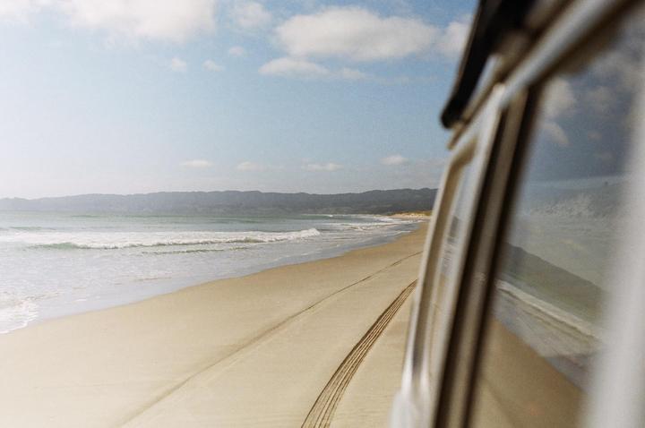 A vehicle is parked on a sandy beach next to the ocean with mountains in the distance.