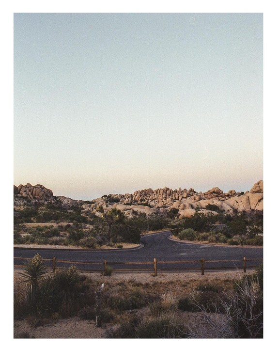 A winding road leads through a desert landscape with large rock formations under a pale sky.