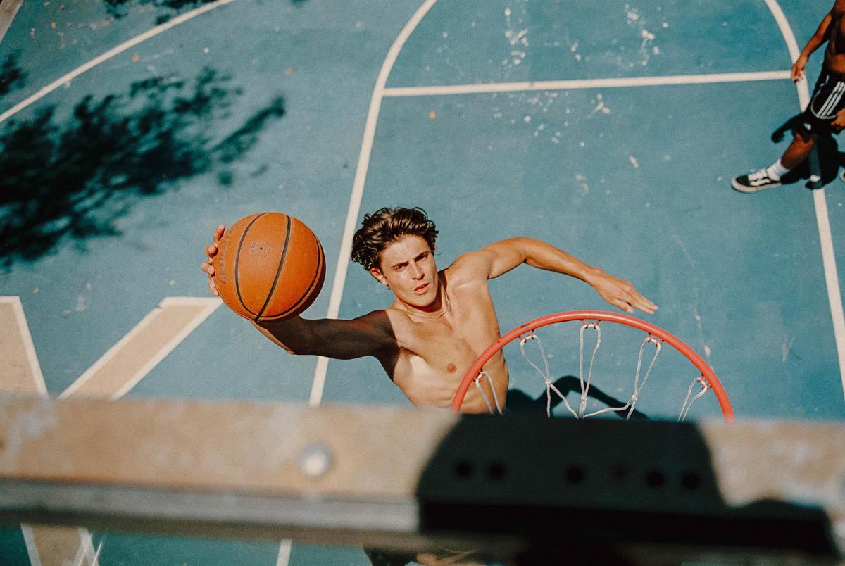 A shirtless man holds a basketball over a hoop on a blue court.