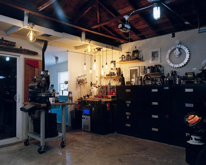 A coffee roasting and brewing setup is visible in a room with exposed wooden beams and industrial lighting.
