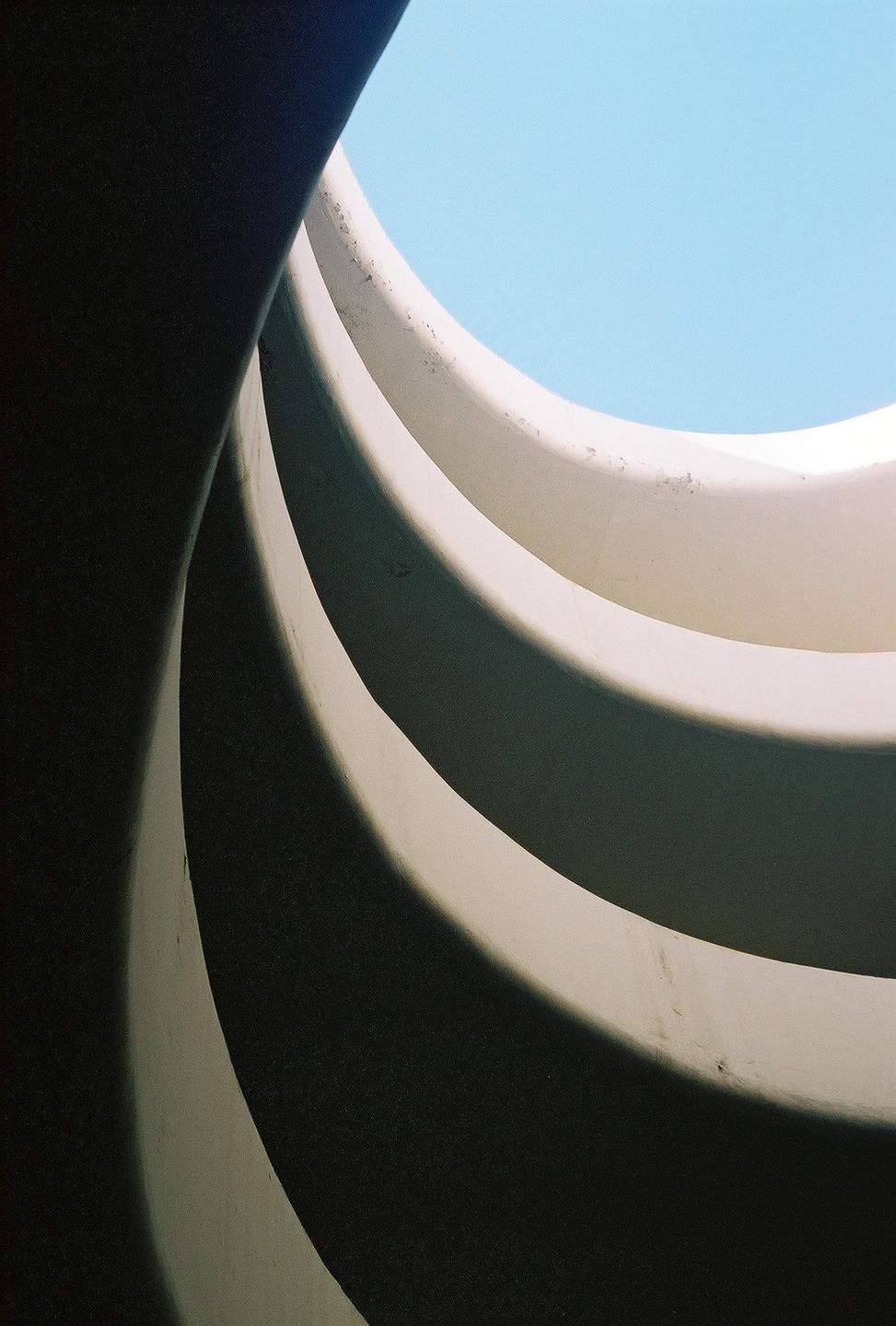 A low-angle shot captures the swirling concrete ramps of a parking garage against a bright blue sky.