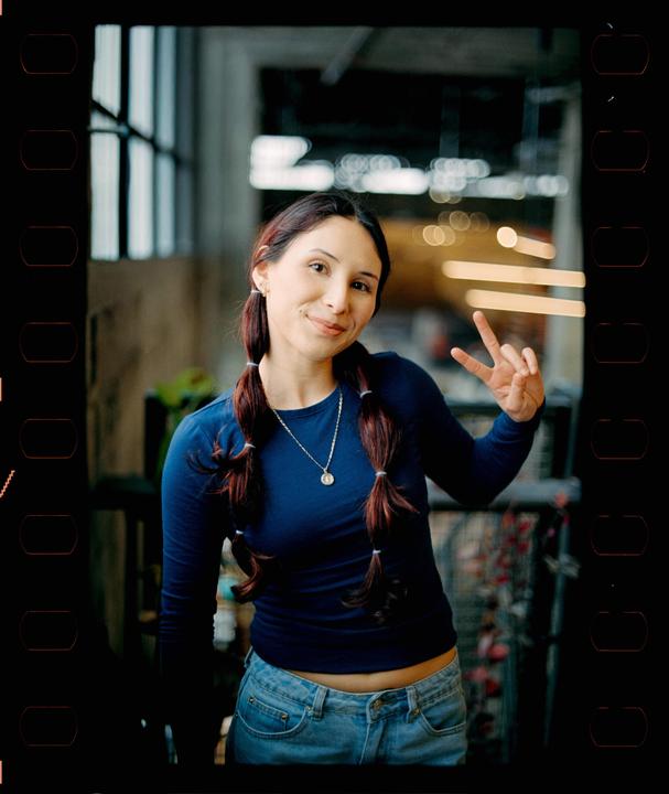 A woman with pigtails and a blue shirt makes a peace sign.
