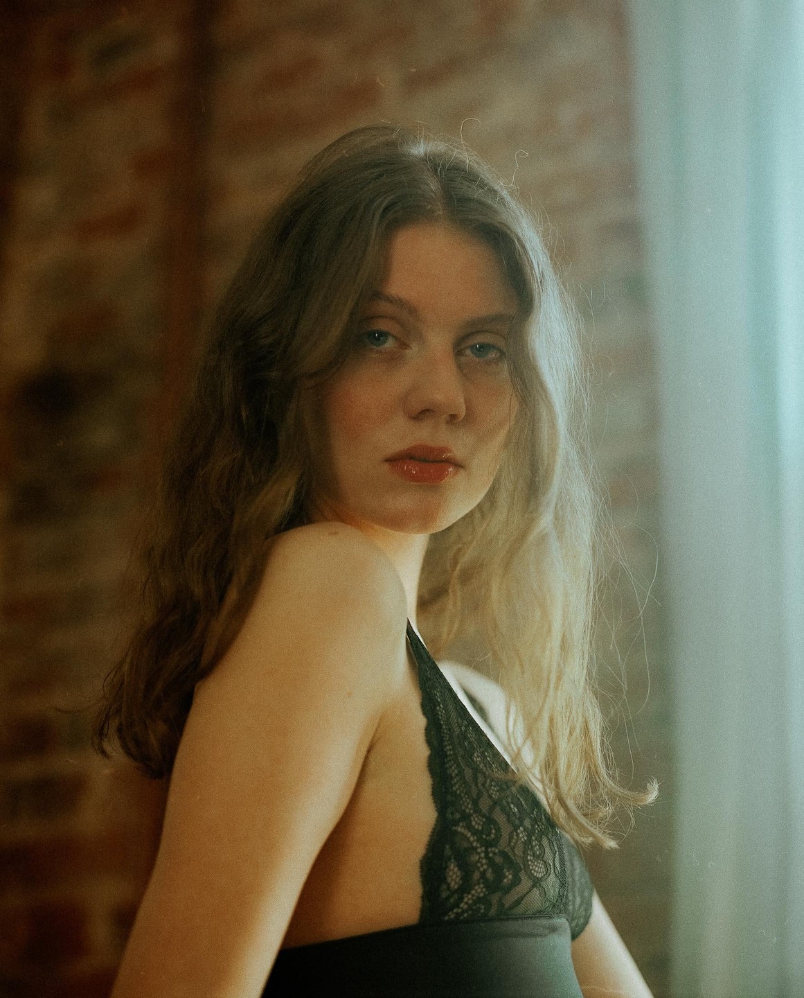 A woman with long wavy hair and a black lace top looks directly at the viewer.