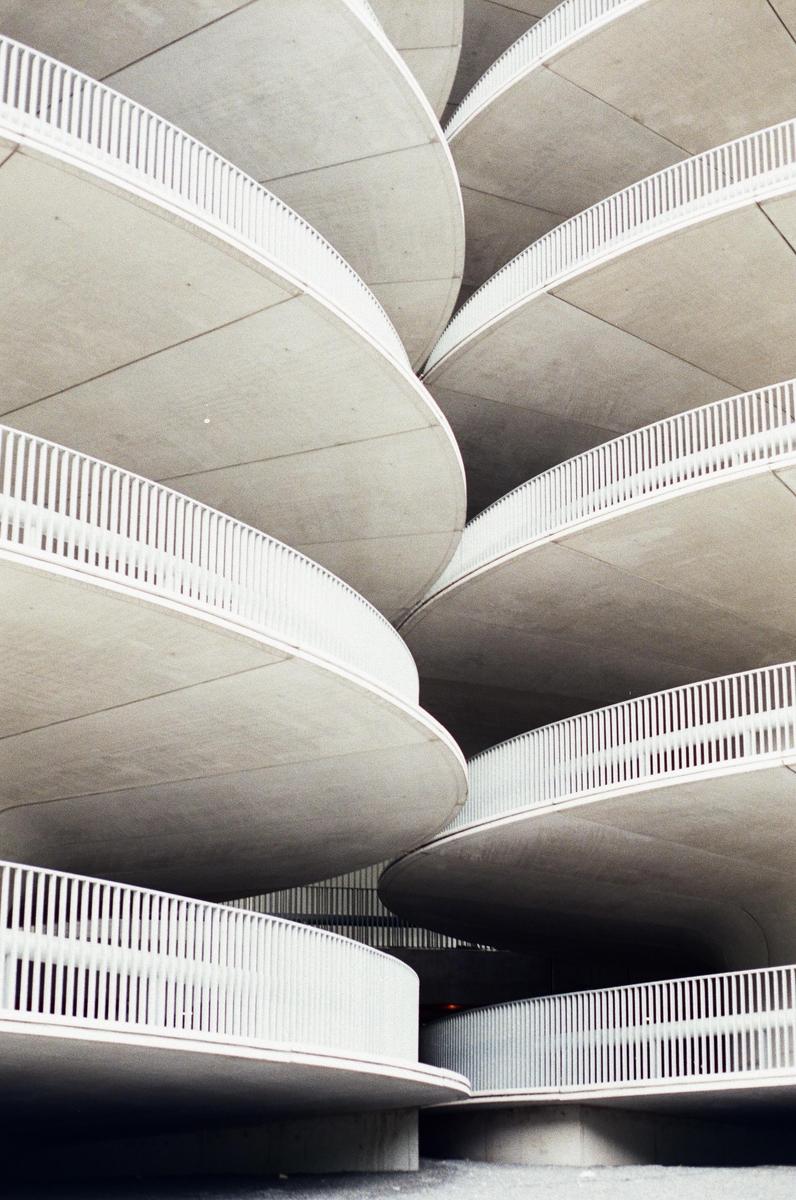 A concrete parking garage features curved ramps and white railings.