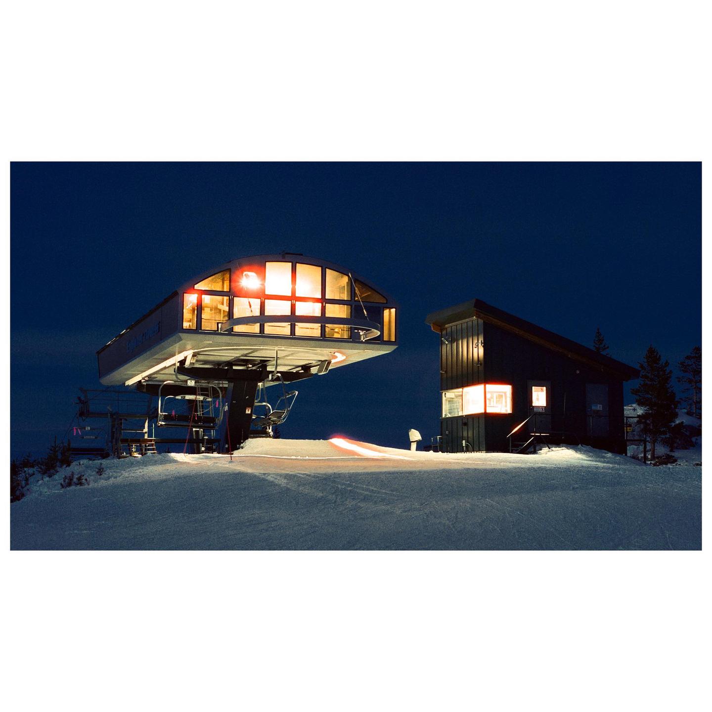 A ski lift station and a building are illuminated at night on a snowy mountain.