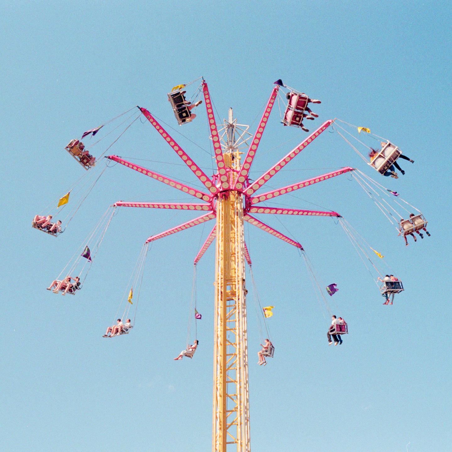 A tall carousel ride with many people in swings is set against a clear blue sky.