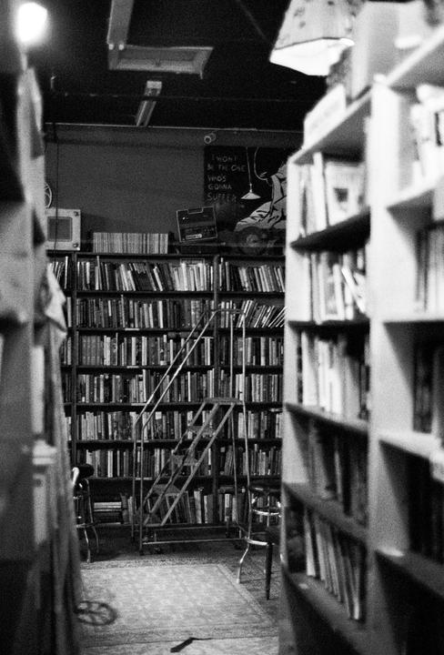 A narrow aisle in a bookstore is lined with tall shelves of books and a rolling ladder.