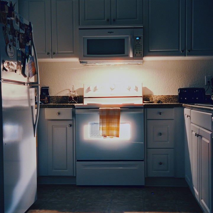 A kitchen with a glowing oven and a refrigerator covered in magnets is shown.