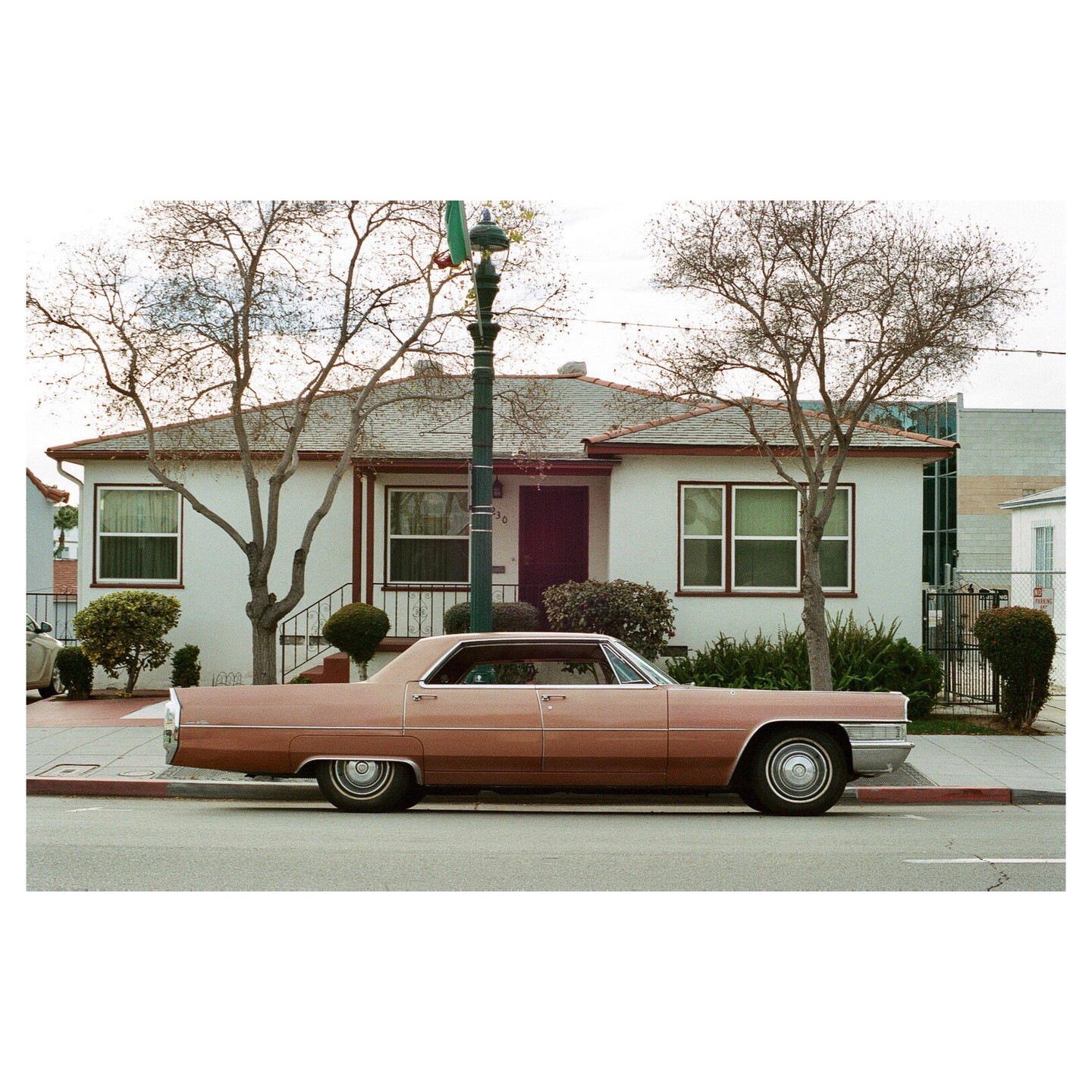 A vintage car is parked on the street in front of a house with bare trees.