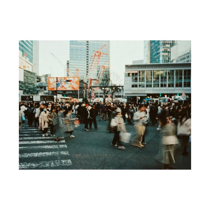 A large crowd of people crosses a street in a city with tall buildings in the background.