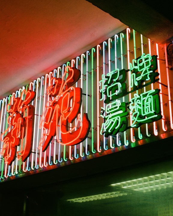 A neon sign with red and green Chinese characters is illuminated against a background of vertical neon tubes.