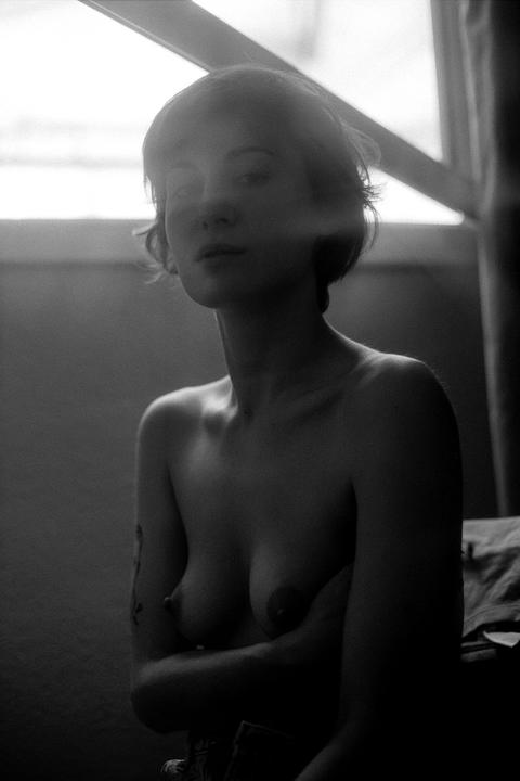 A woman with short hair is shown from the chest up, with her arms crossed over her chest, in front of a window.