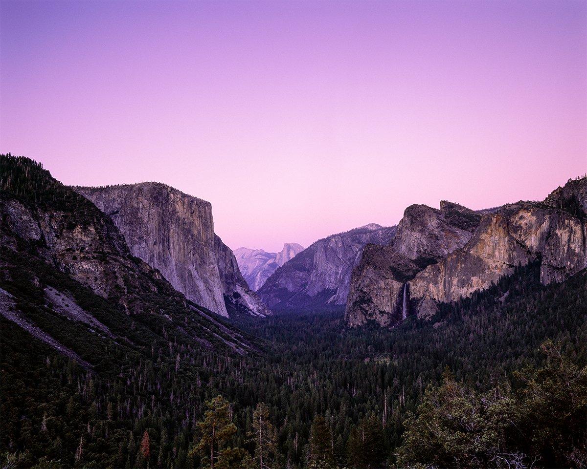A valley with a forest and mountains is visible under a purple sky.