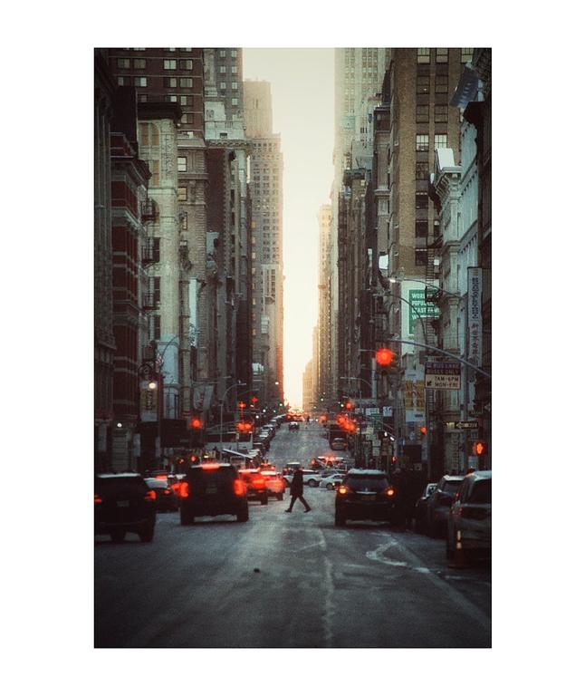 A person crosses a busy street lined with tall buildings and cars with glowing red taillights.