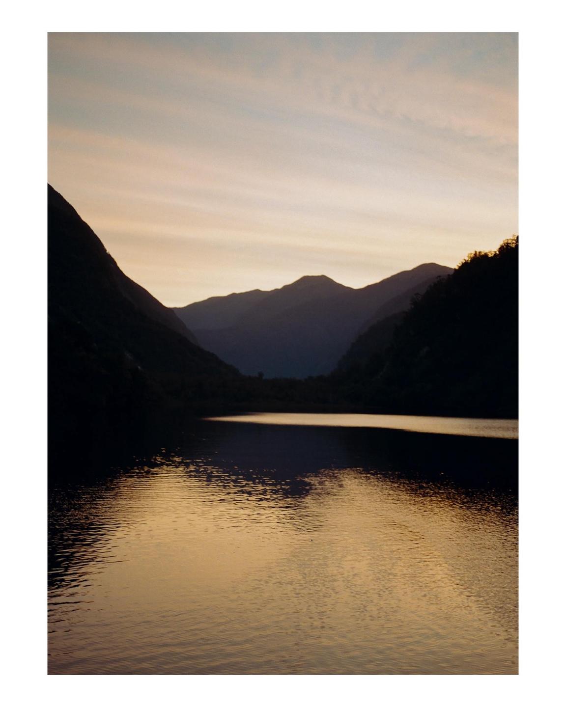 A body of water reflects the sky and mountains at dusk.