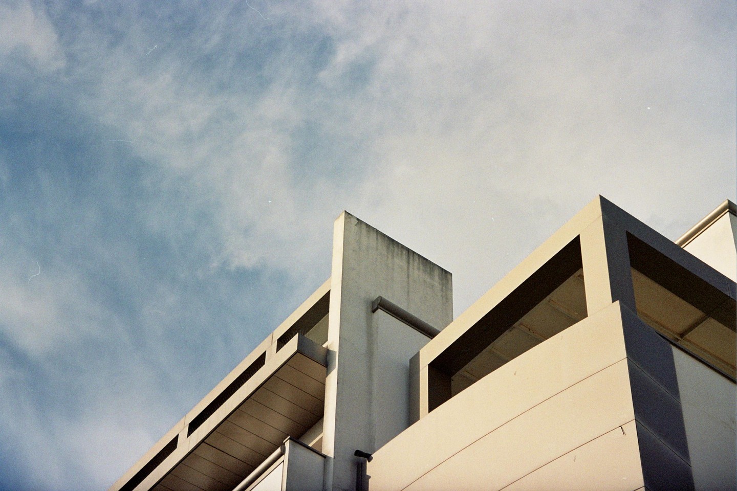 A low-angle view shows the geometric architecture of a building against a cloudy sky.