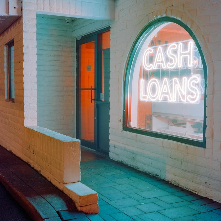 A neon sign for "CASH LOANS" glows in an arched window next to a doorway with an orange-lit interior.