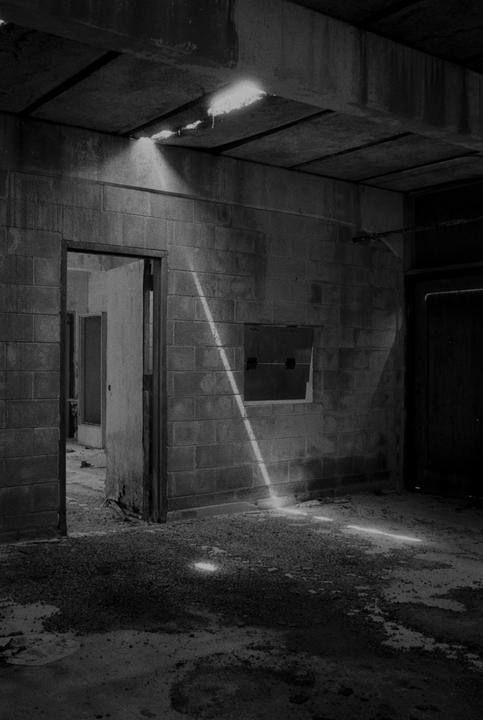 Sunlight streams through holes in the ceiling of a derelict building, illuminating dust and debris on the floor.
