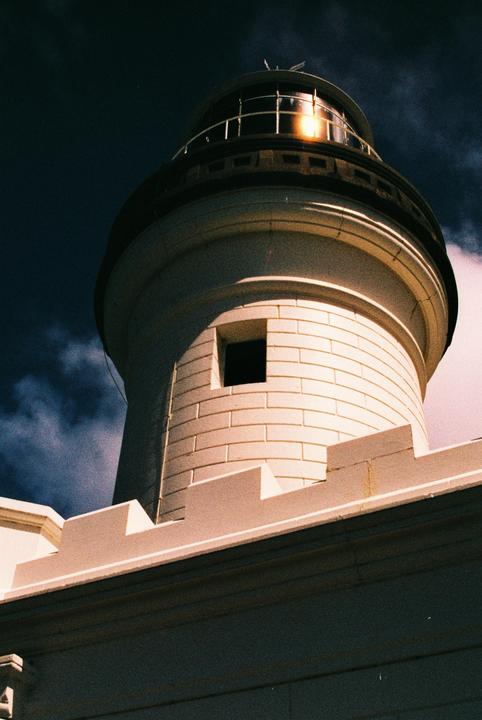 A white lighthouse with a dark sky and a bright light in its lantern room is shown from a low angle.