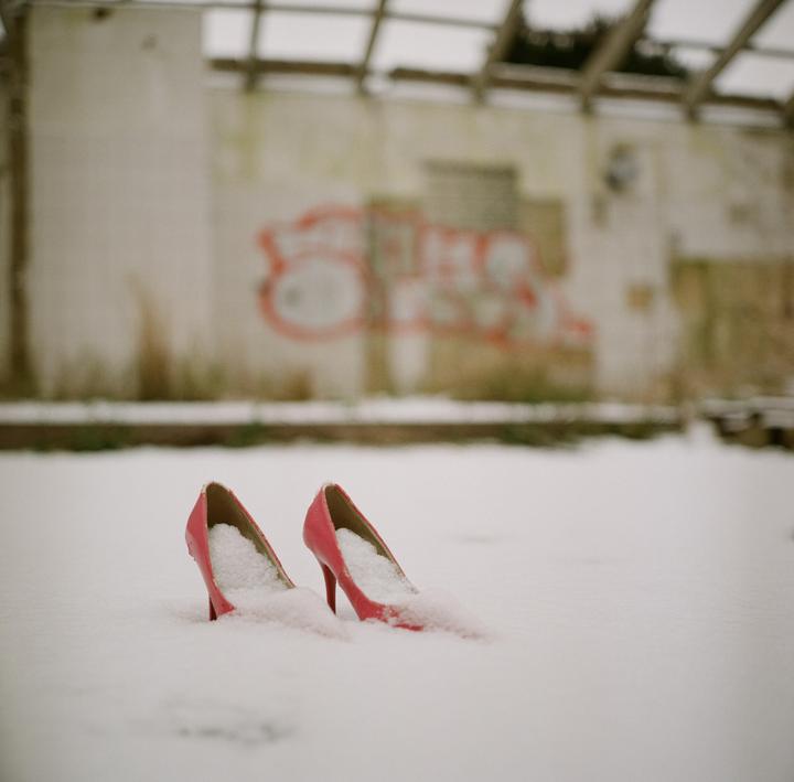 Two pink high heels are partially buried in snow in front of a building with graffiti.