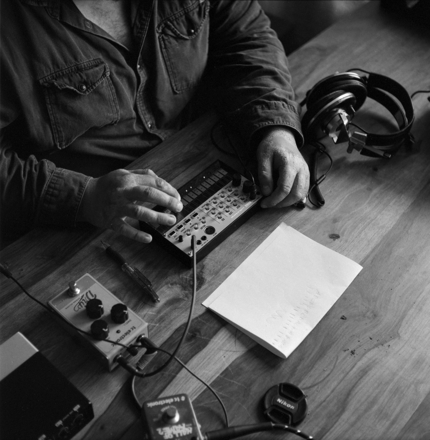 A man is playing an analog synthesizer on a wooden table.