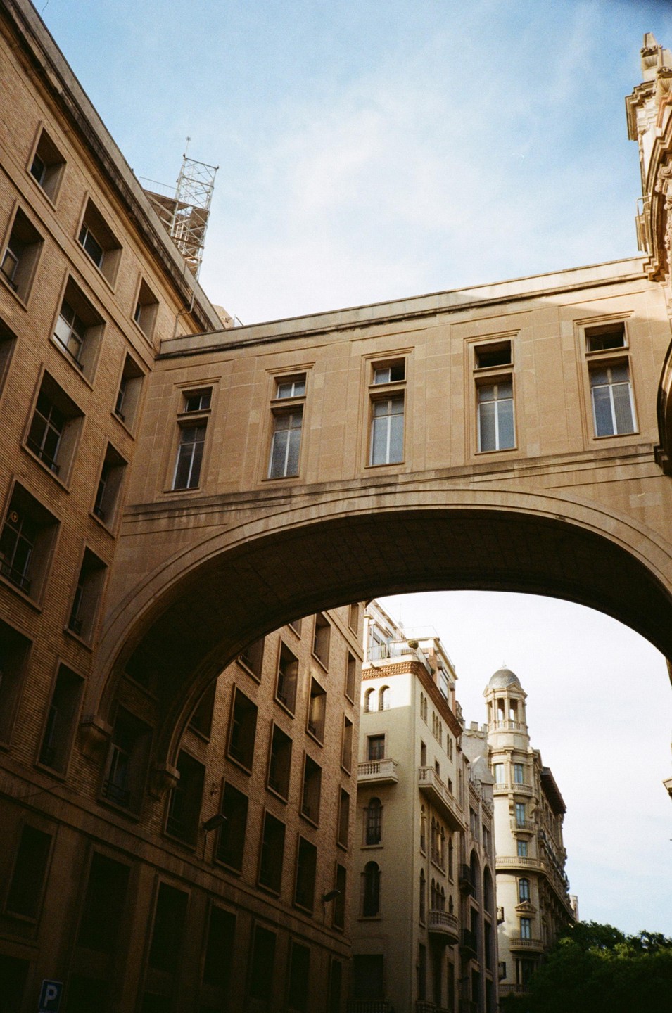 A stone archway connects two buildings under a bright sky in Barcelona.