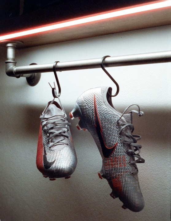 Two silver and red athletic shoes hang from a metal bar with a red neon light above them.