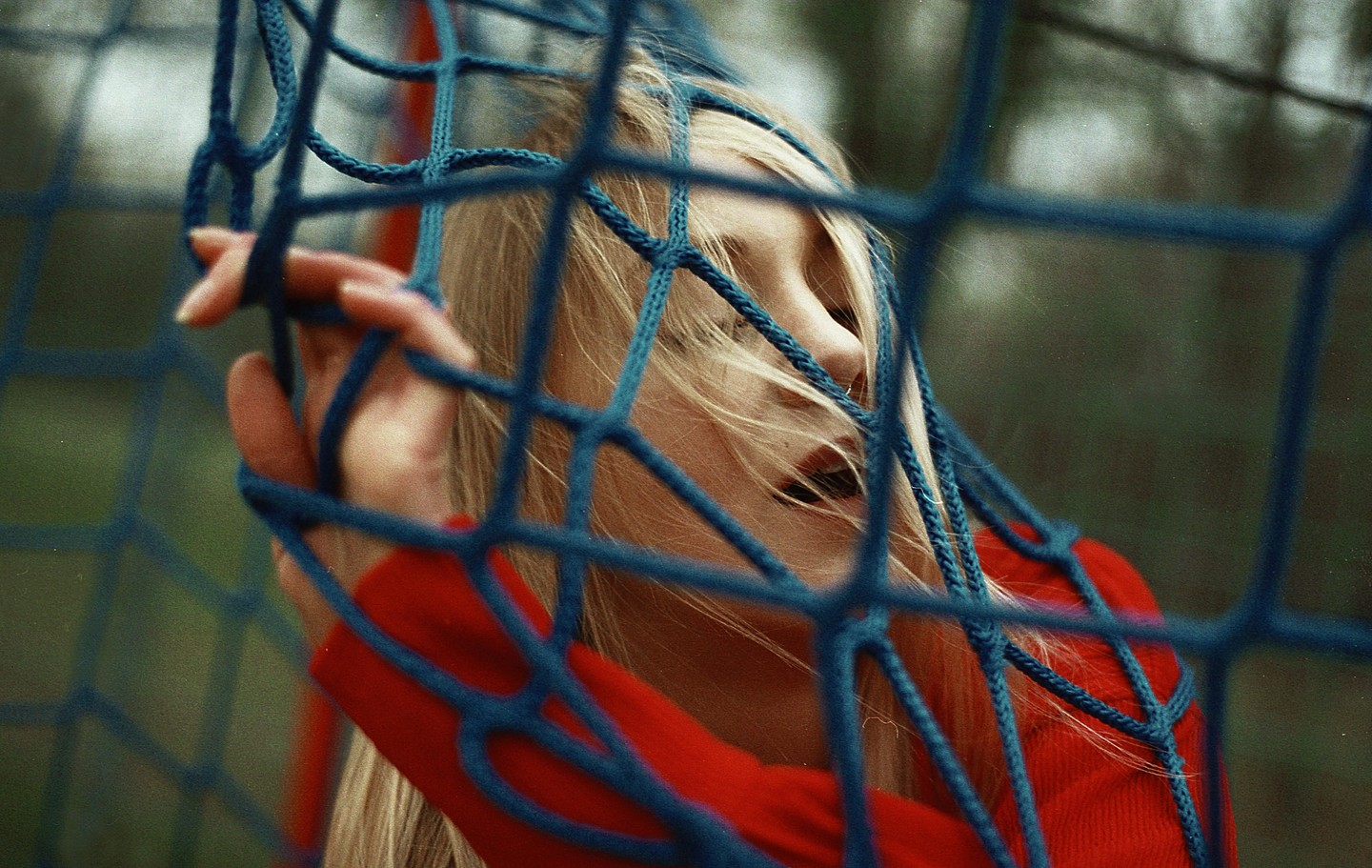 A young woman with blonde hair and a red shirt is visible through a blue net.