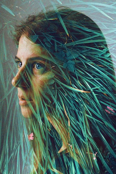 A woman's face is visible through a double exposure with tall green grass and small pink flowers.
