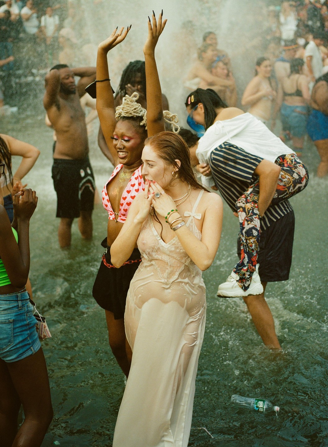 A group of people are celebrating in the water at Washington Square Park, with one woman in a wet dress and another with her arms raised.