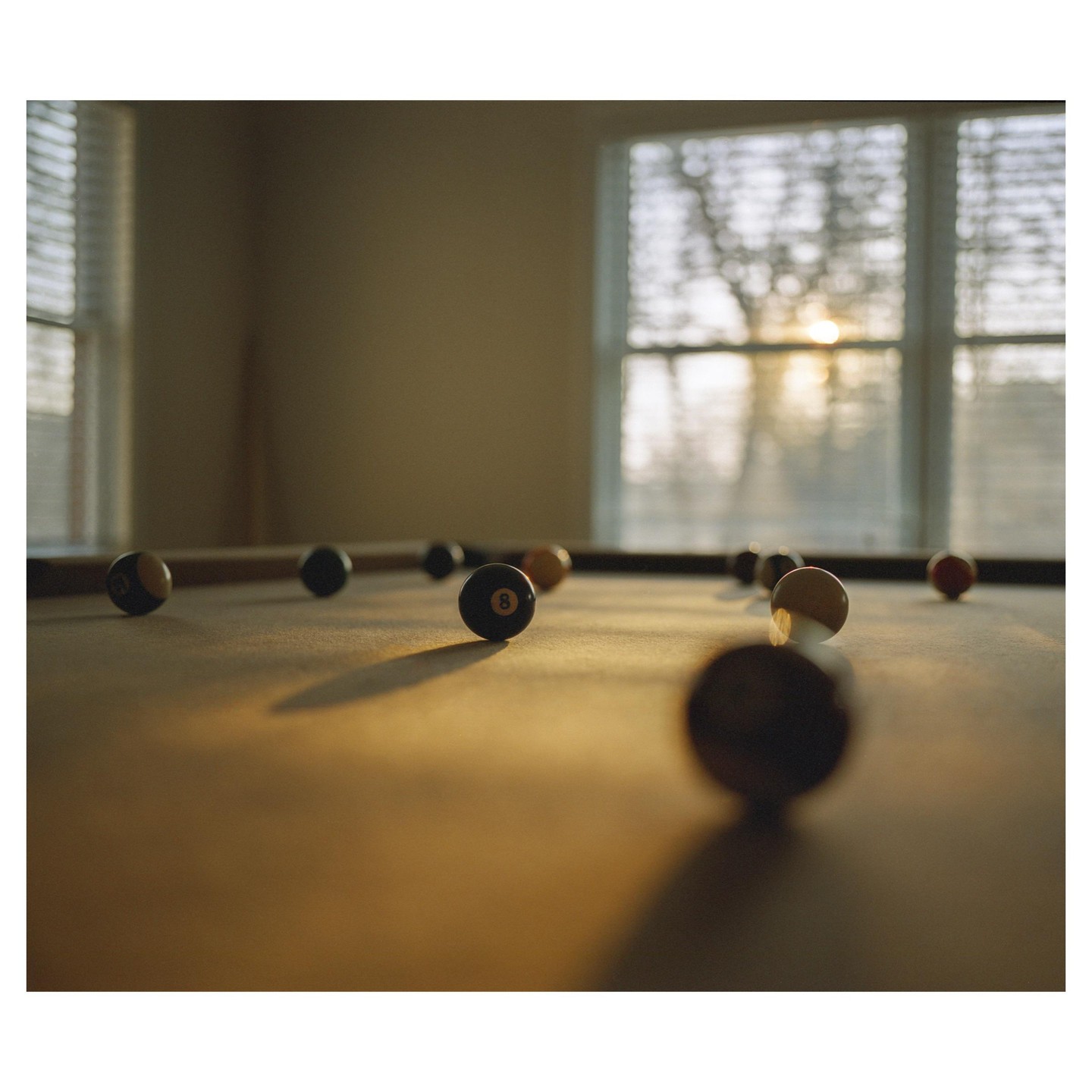 Pool balls are scattered across a pool table with sunlight streaming through a window in the background.