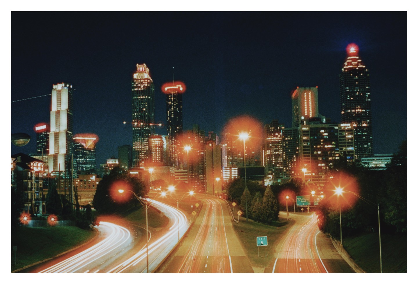 A long exposure shot of a city skyline at night with light trails from cars on a highway.