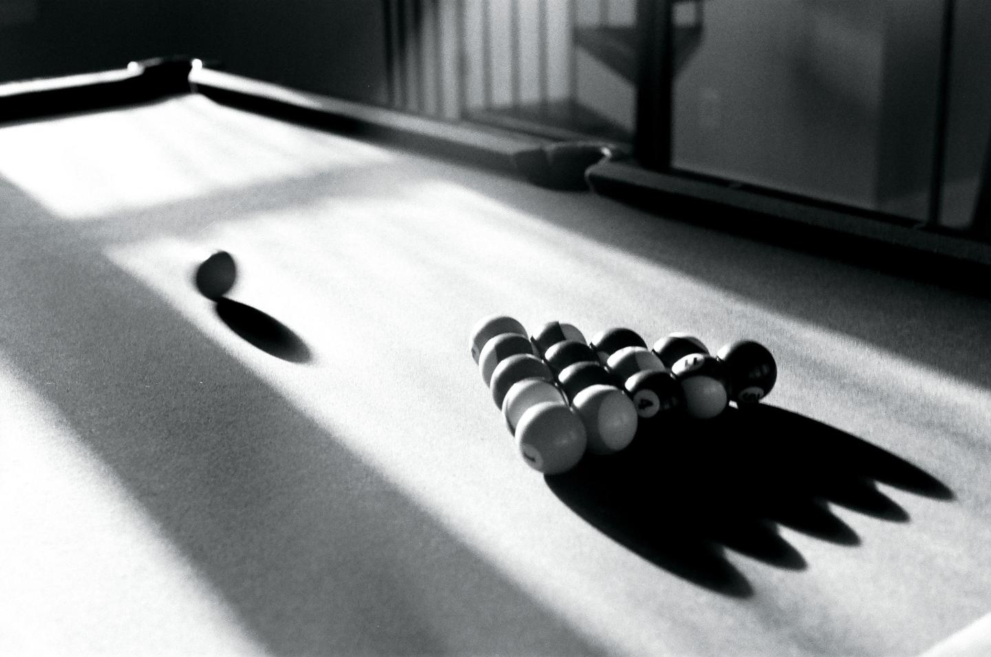 A cue ball and racked billiard balls cast long shadows on a pool table.