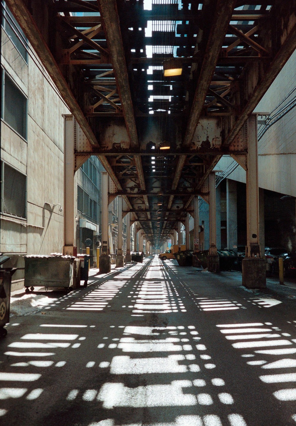 A long alleyway is covered in shadows from an elevated train track in Chicago.